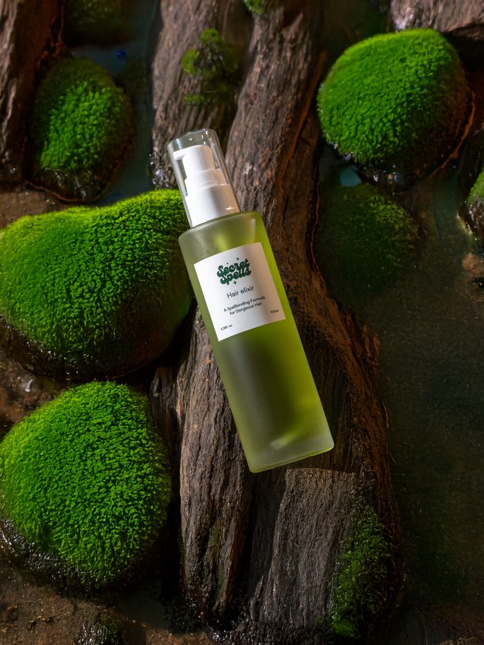 Green hair oil bottle surrounded by lush moss and rocks, embracing nature.