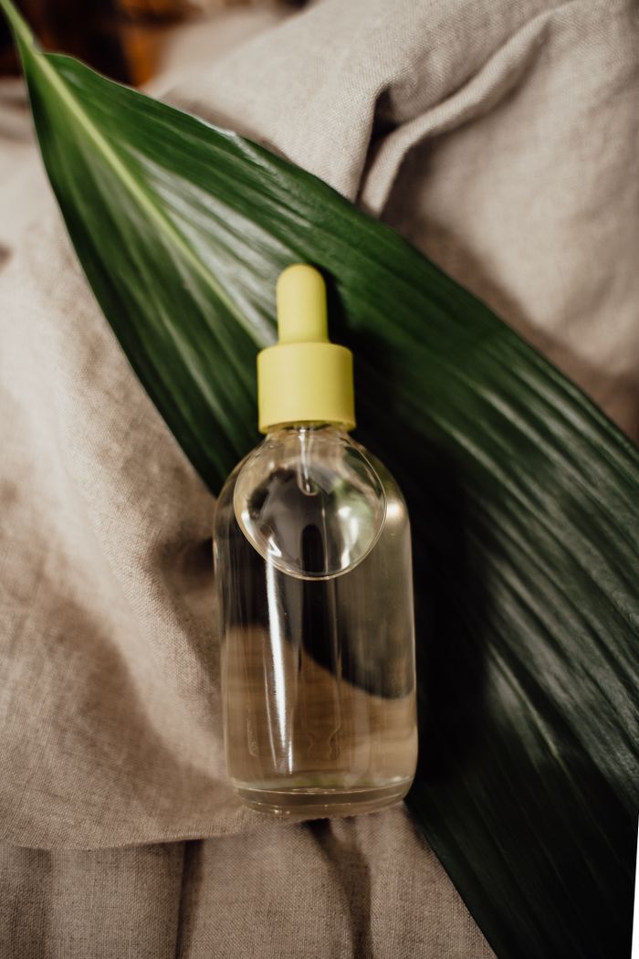 Glass dropper bottle of cosmetic serum on a green leaf for eco-friendly skincare.