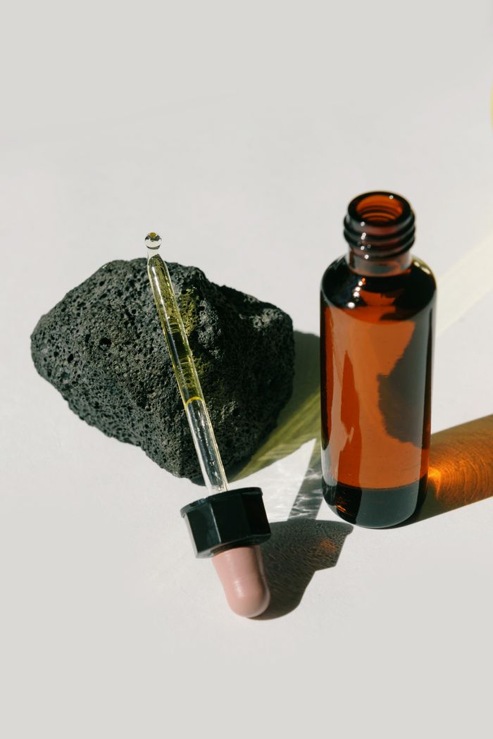 Amber glass dropper bottle and textured lava rock on white background under sunlight.